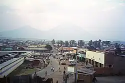 Photograph of Ruhengeri, Rwanda, with buildings, a street, and people visible, and mountains in the background, partially in cloud