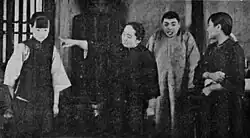 A black-and-white image of a man pointing at a woman, with two others to his right
