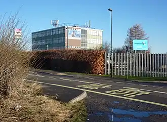 Roadside with bus stop in foreground and slab sided multi storey modern building with large windows behind on a sunny day with a bright blue sky