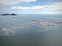 A patch of land being reclaimed from the sea, with an island visible in the background.