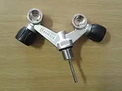 a parallel thread cylinder valve is shown, with a chromed dip tube, and two DIN valved connection sockets. The sockets are offset from the angled arms of the valve body, which branch at roughly 45 degrees from the neck thread axis in the same plane. The connection socket axes are orthogonal to the plane of the arms, and the valve spindles are orthogonal to their outlets and the axis of each arm, with the knobs to the outsides.