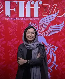 33 jährige Frau von prunkvoll gestaltetem Plakat des Fajr-Festivals, stehend mit verschränkten Armen, Kopftuch tragend, freundlich lächelnd