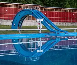Two blue body slides, similar to playground slides, on the far side of a swimming pool