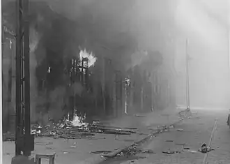 IPN copy #48 (No image caption, in section This is how the former Ghetto looks after having been destroyed) Zamenhofa Street between Wołyńska and Miła looking North, with burning Zamenhofa 29, 31 and 33 on the left.