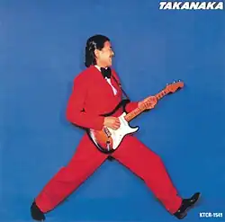 Blue background with Takanaka taking a large step in a red suit with guitar in hand