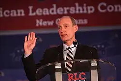 McCotter stands at a podium with his right arm bent at the elbow and facing up