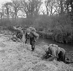 Soldiers from the division training, take cover along a river bank.