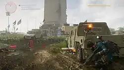 A horizontal rectangular video game screenshots that depicts a virtual representation of a battle field. A soldier in the foreground hides behind an armored vehicle with a small gun mounted on its top. In the background is the base of a large obelisk and tattered flags flying on flagpoles.