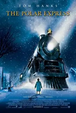 At night in a snowy neighborhood street, a boy stands in front of a large steam locomotive that is placed in the middle of the road.