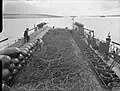 At Scapa Flow, a Royal Navy net laying vessel prepares to lay an anti-submarine net, which is 900 feet (270 m) long, weighs over 40 long tons (41 t) and could be laid in 4 minutes.