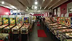 Most of the pinball machines are lit up and ready to play, except for a couple with the playing field opened up for repairs. Informative signs stand on top of each machine, describing its history and importance. It's night and attendance at the museum is relatively light.