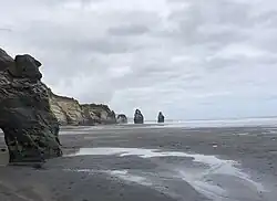An image of three distant sea stacks from the river mouth on a beach