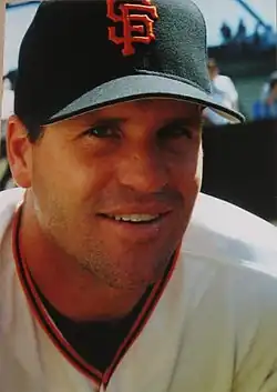 A smiling man with a 5 o'clock shadow wearing a black baseball cap with an interlocking "SF" on the front