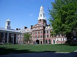A college courtyard; a large brick building with a tall white spire is visible to the right