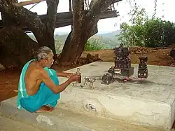 a man in blue/turquoise clothes sitting in front of small figures of gods.