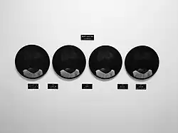 The head and shoulders of a black woman in a simple white cotton shift, taken from the back leaving the subject unknown. The black and white photographs are alongside six engraved text plaques and fixed directly to the wall. One text plaque hangs above the photographs and five are placed below.