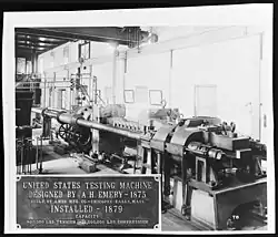 A large machine with a sign that reads “United States testing Machine Designed by A. H. Emery – 1879. Built by Ames MFG. Co. – Chicopee Falls, Mass. Installed – 1879. Capacity 800,000 LBS. Tension – 1,000,000 LBS. Compression.”