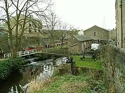 An urban beck; a stream with footbridge over it among several sandstone buildings