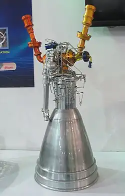 A physical model of a spacecraft engine, with a curved semi-cylindrical structure at the bottom, a flat cylindrical structure in the middle, a silver-colored inlet and two red and gold-colored pipes at the top.
