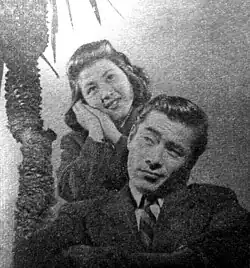 Yoshiko Kuga stands above and behind Toshiro Mifune.
