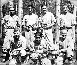 A black-and-white photograph of a group seven young campers posing in their baseball uniforms.