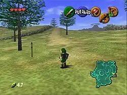 The child version of the game's protagonist, Link, stands in Hyrule field wearing his distinctive green tunic and pointed cap. In each corner of the screen are icons that display information to the player. In the upper left-hand corner, there are hearts, which represent Link's health, in the lower left-hand corner is a counter that displays the number of Rupees (the in-game currency) possessed by the player. There is a mini-map in the lower right-hand corner, and five icons in the upper right-hand corner, one green, one red, and three yellow, which represent the actions available to the player on the corresponding buttons of the N64 controller.