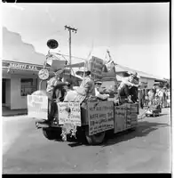 Float with multiple signs at the Bangtail Muster, 1963